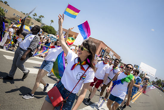 Group of happy people marching in the annual San Diego Pride parade - the person at the front of the photo is waving a rainbow flag